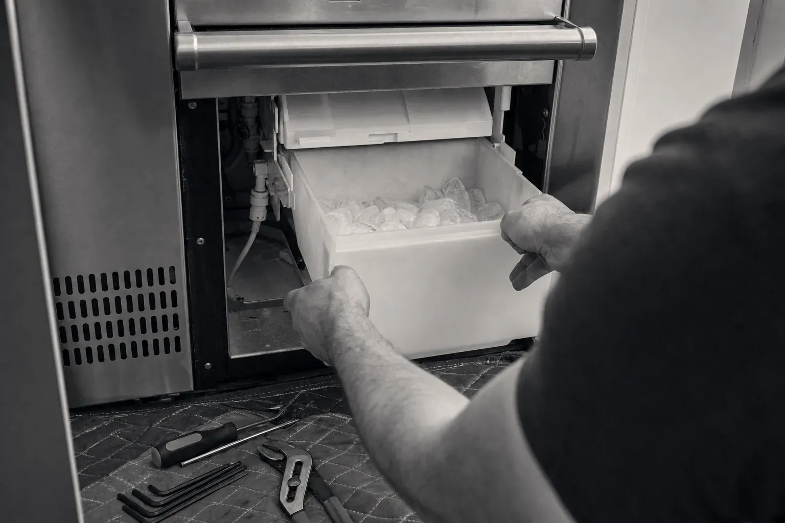Technician pulling the ice bin from an under-counter ice maker, hand tools on floor