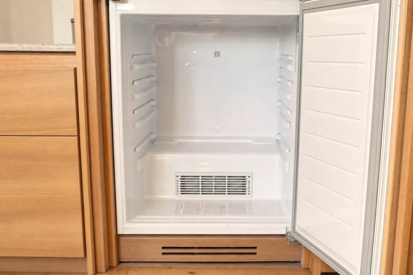 Empty under-counter refrigerator with shelf rails and rear vent grille