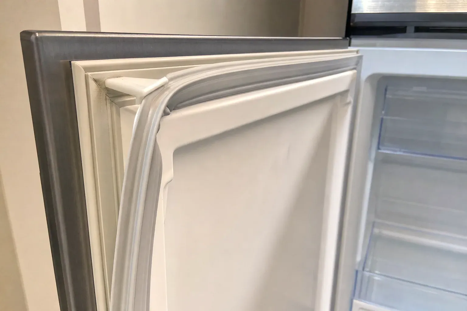 Close view of a white door gasket at the corner of an open refrigerator door