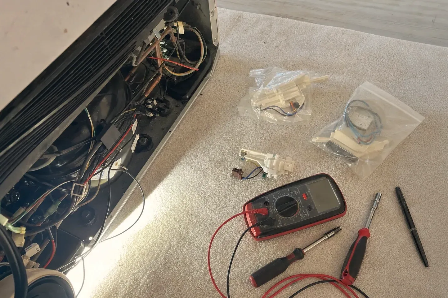 Multimeter, screwdrivers and bagged relay parts on carpet by an open compressor bay