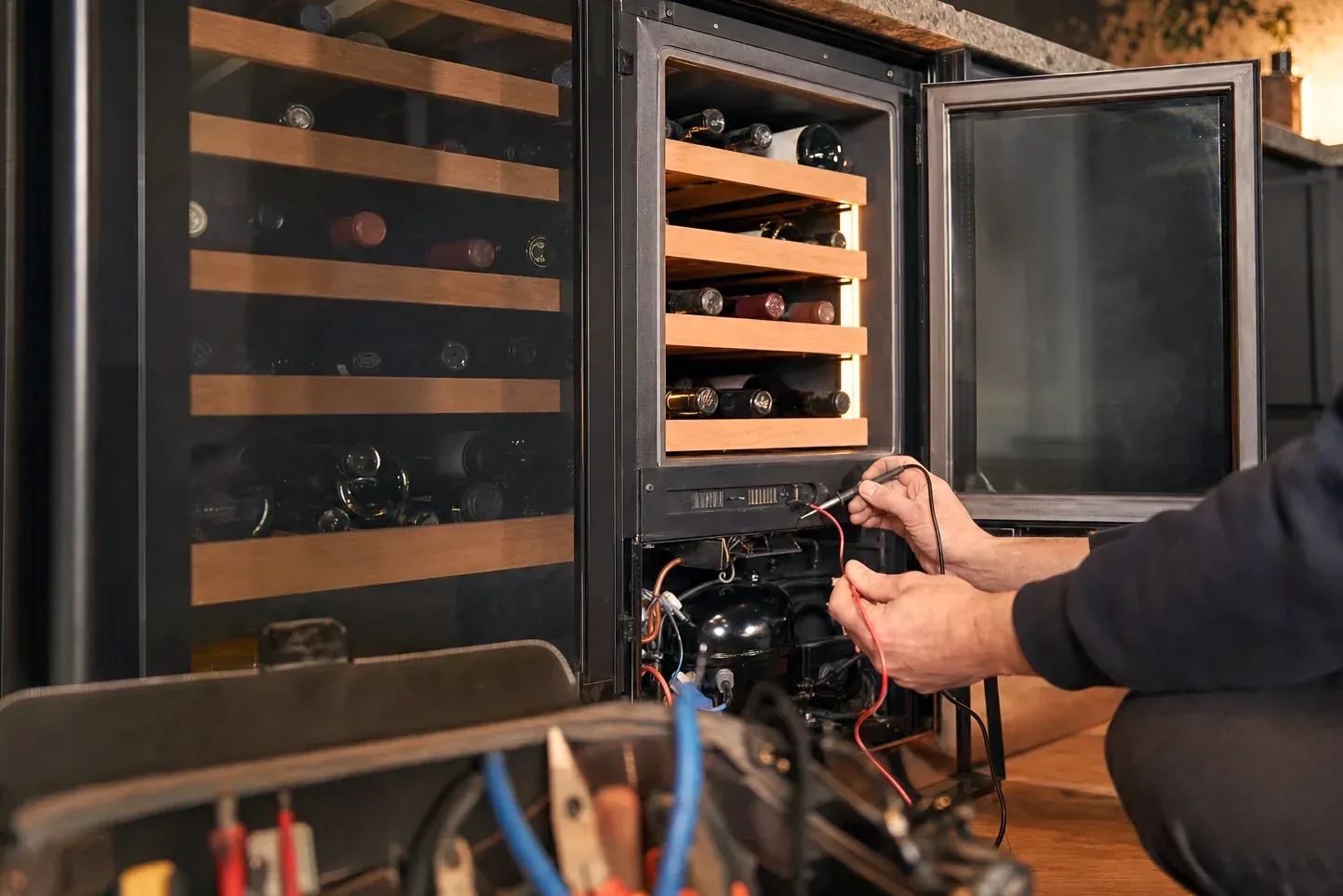 Technician testing wiring at the base of a wine cooler with meter leads