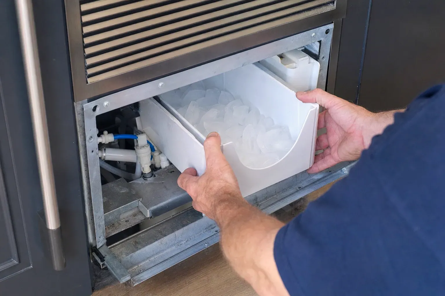 Technician removing an ice bin full of cubes from an under-counter ice maker