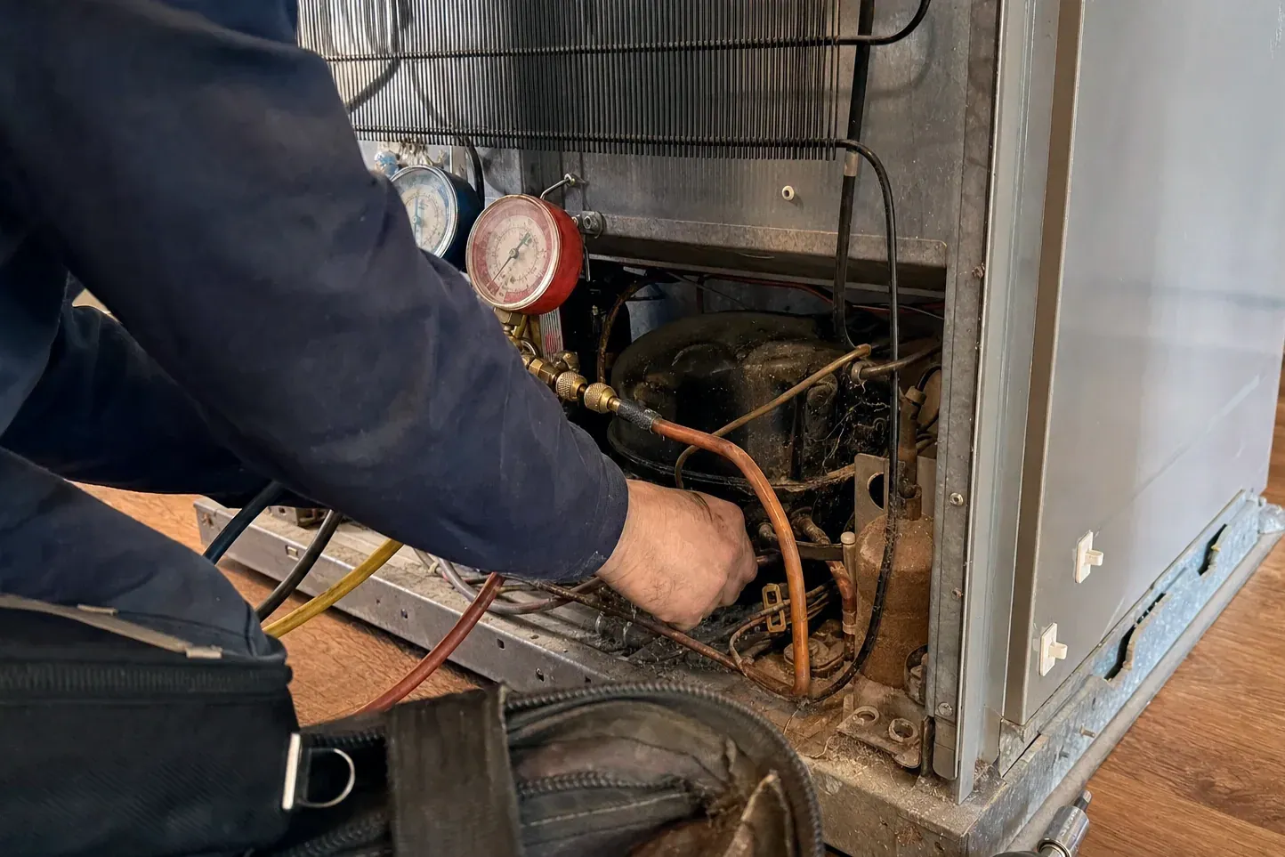 Technician reaching into rear compressor bay with refrigerant gauges attached