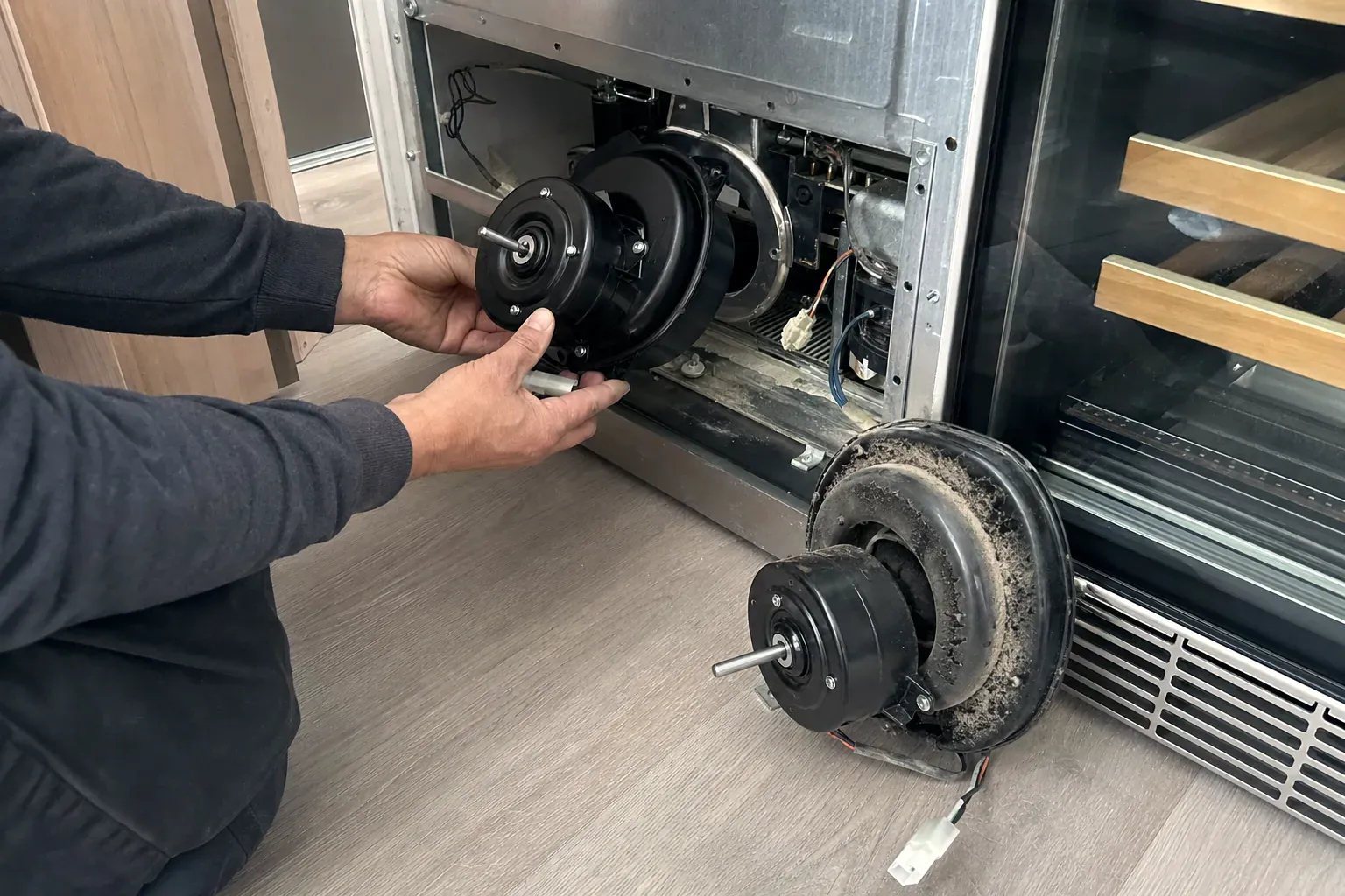 Hands holding a new evaporator fan motor beside the dust-caked old one