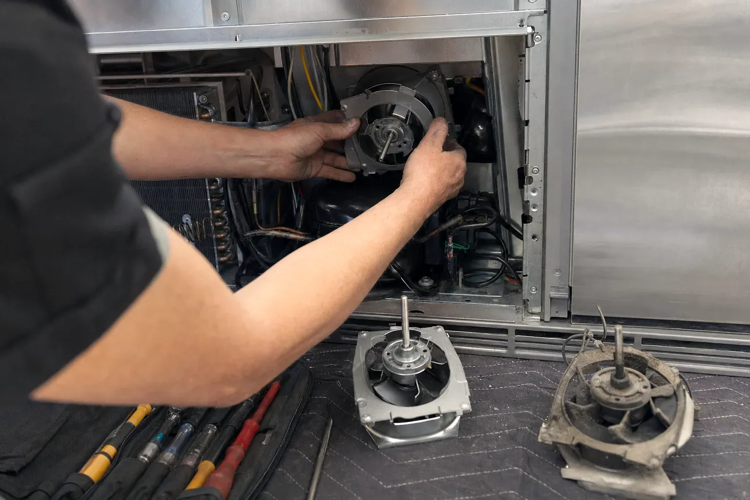 Technician installing a condenser fan motor with two removed motors on a mat