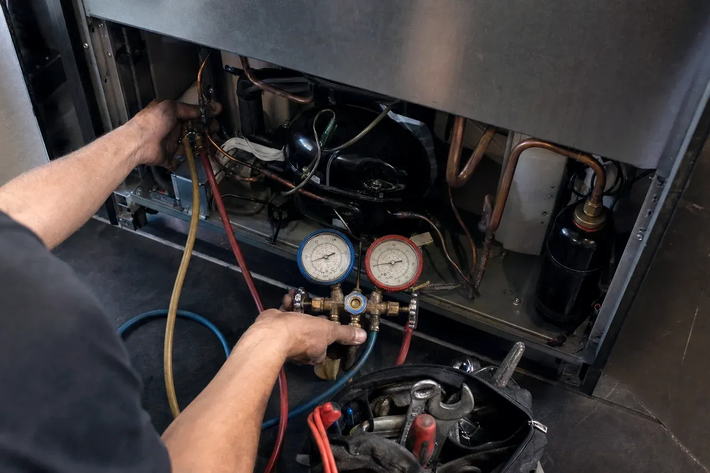 Technician connecting refrigerant manifold gauges to a refrigerator compressor compartment