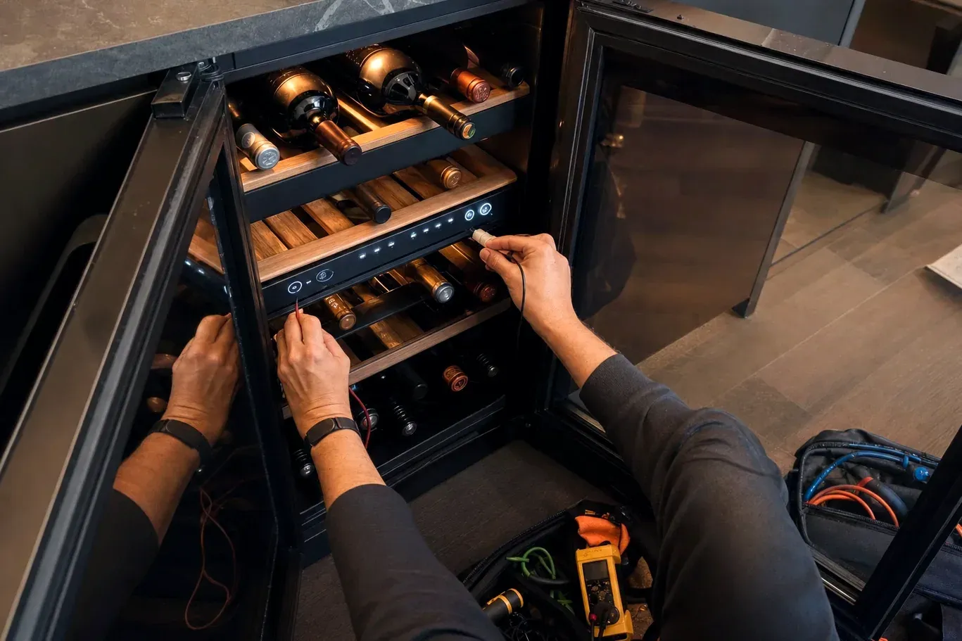 Technician probing the control panel of a wine cooler holding bottles on wood shelves
