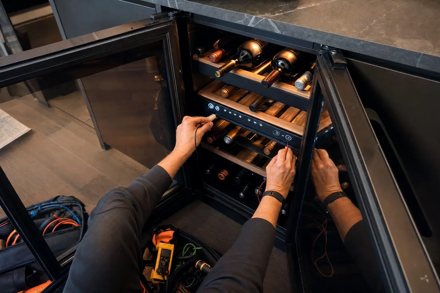 Technician testing a wine cooler control panel with meter leads, tool bag on the floor