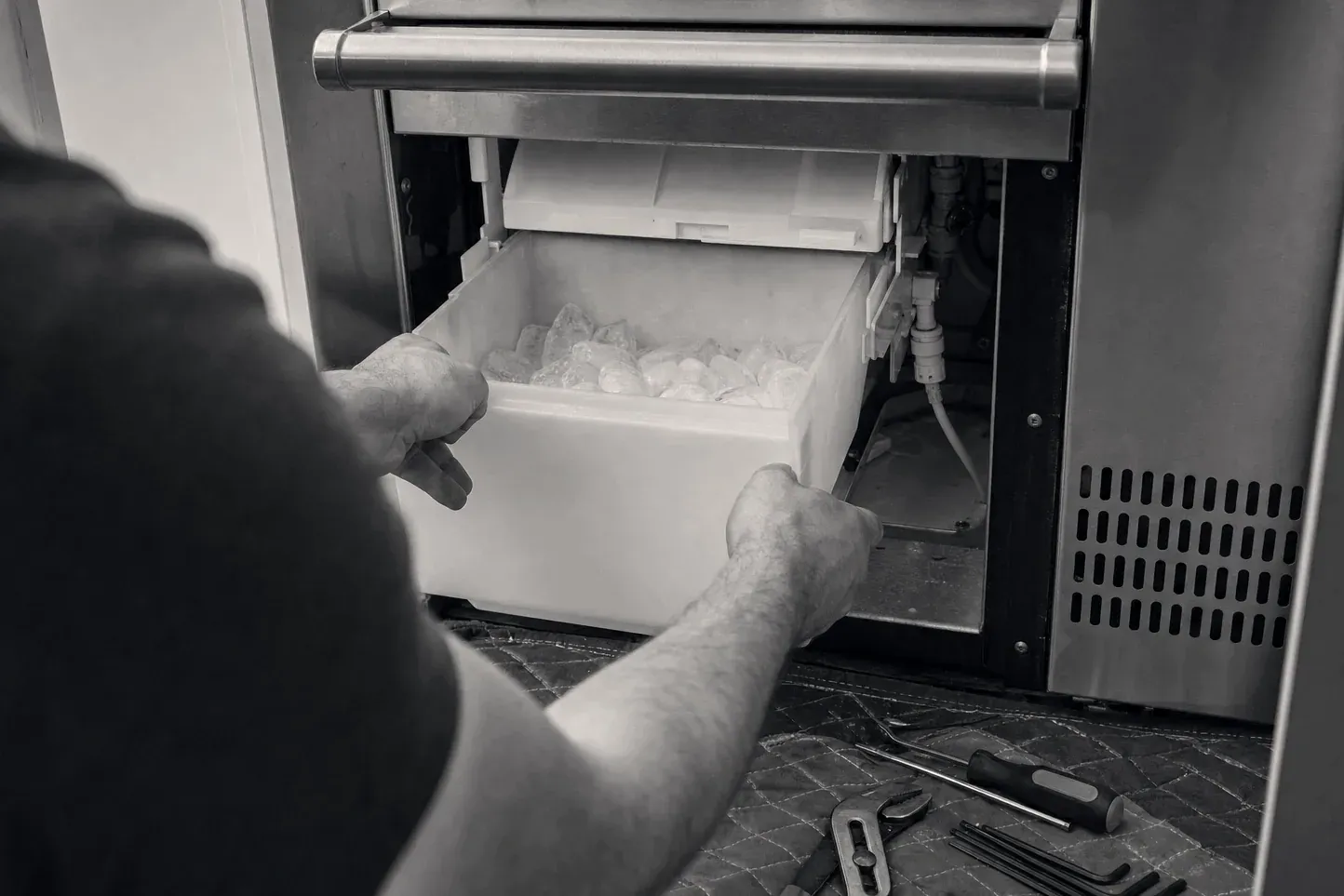 Technician pulling out an ice maker bin with tools on the floor