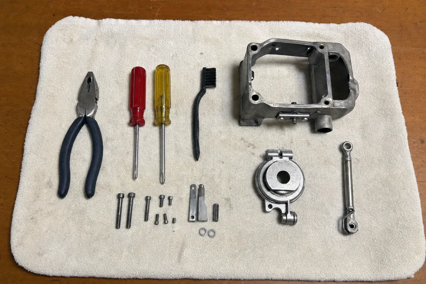 Cast metal housing, linkage rod, screws, screwdrivers and pliers on towel