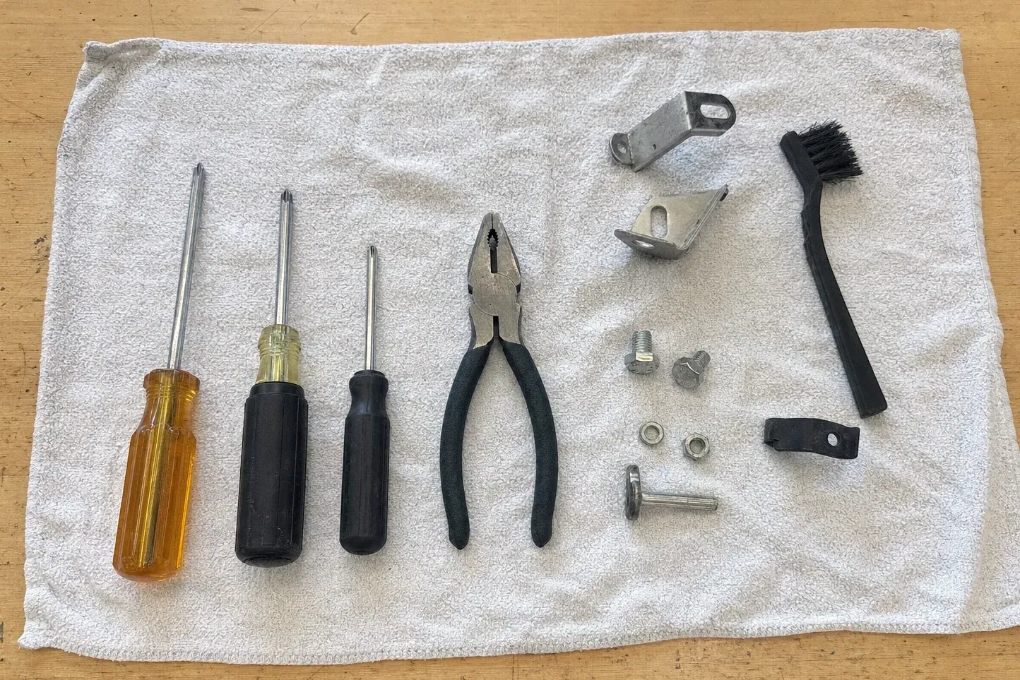 Black brush, brackets, bolts, pliers and three screwdrivers on towel