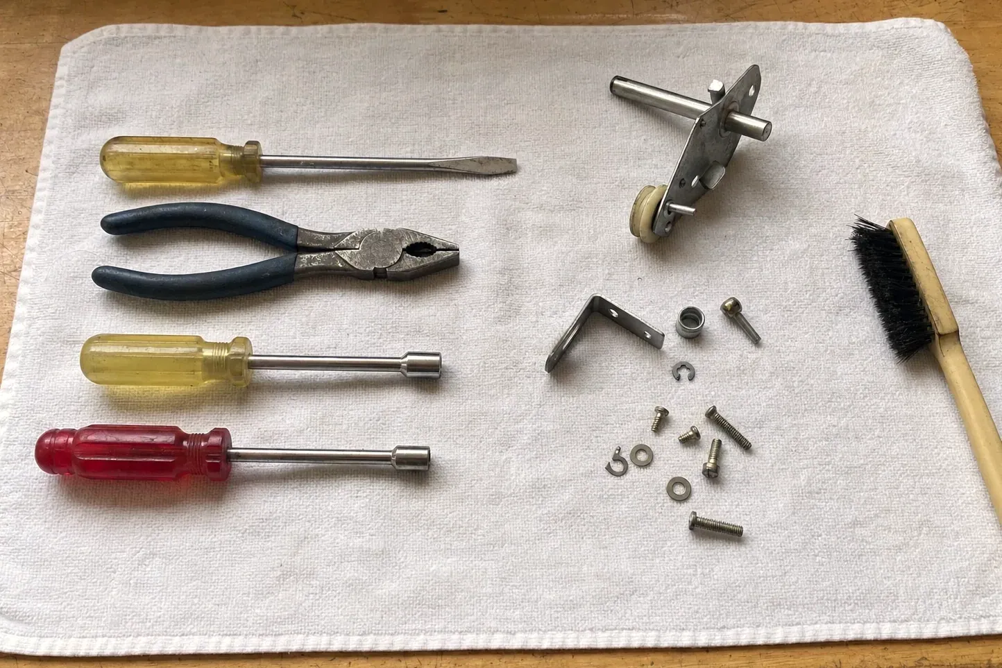 Roller shaft bracket and small fasteners beside screwdrivers and pliers