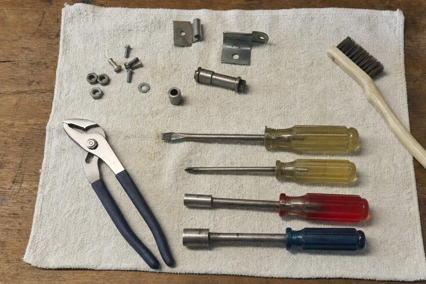 Screwdrivers, pliers, brush and small brackets laid on a rag