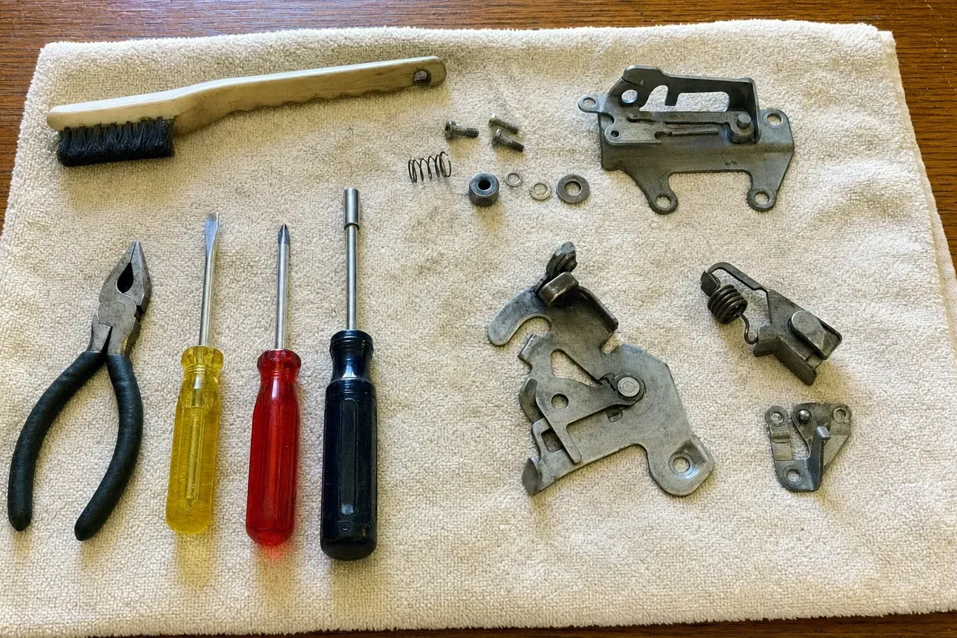 Disassembled latch mechanism with screwdrivers, brush and pliers