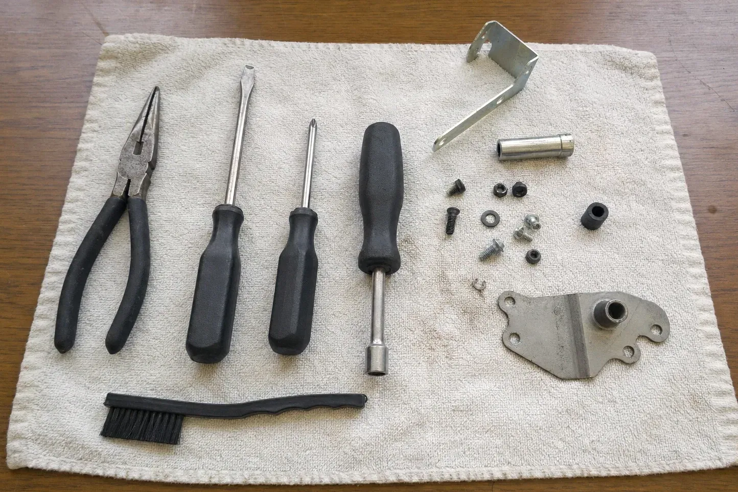 Bracket, sleeve, nuts, three screwdrivers, pliers and brush on towel