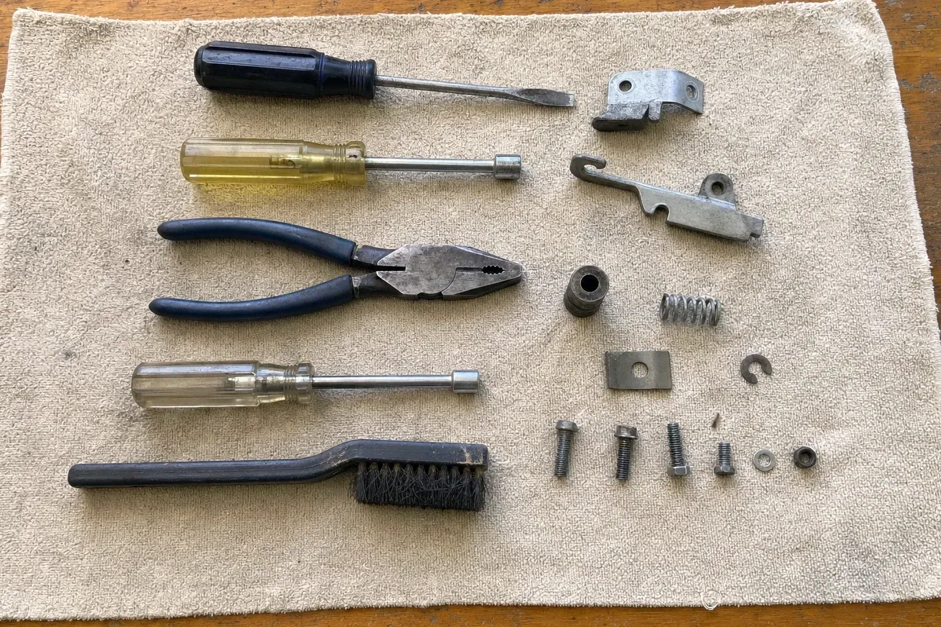 Metal latch parts beside screwdrivers, pliers and brush on cloth