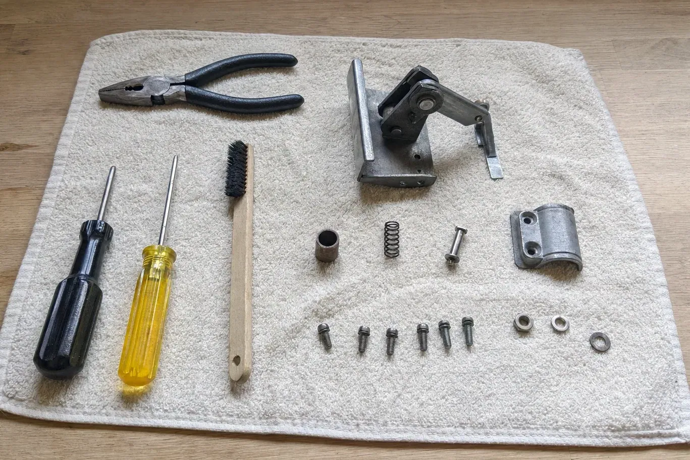Disassembled metal hinge assembly with screws and hand tools on towel