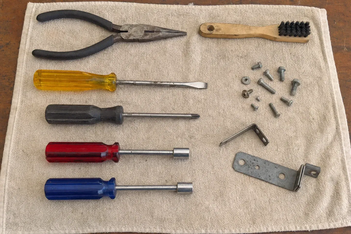 Wooden brush, pliers, screwdrivers, screws and brackets on a towel