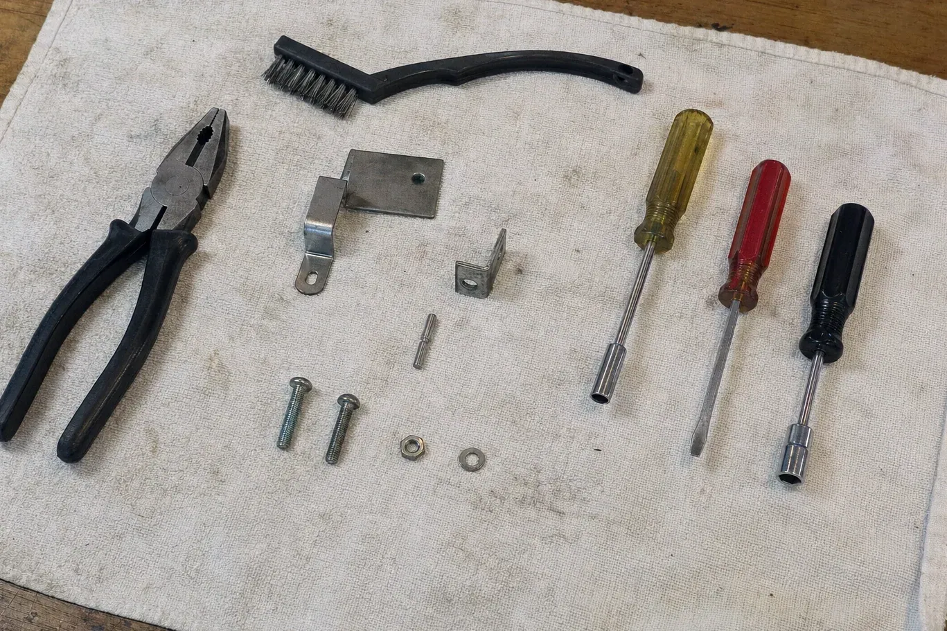 Three screwdrivers, brush, pliers and small metal brackets on cloth
