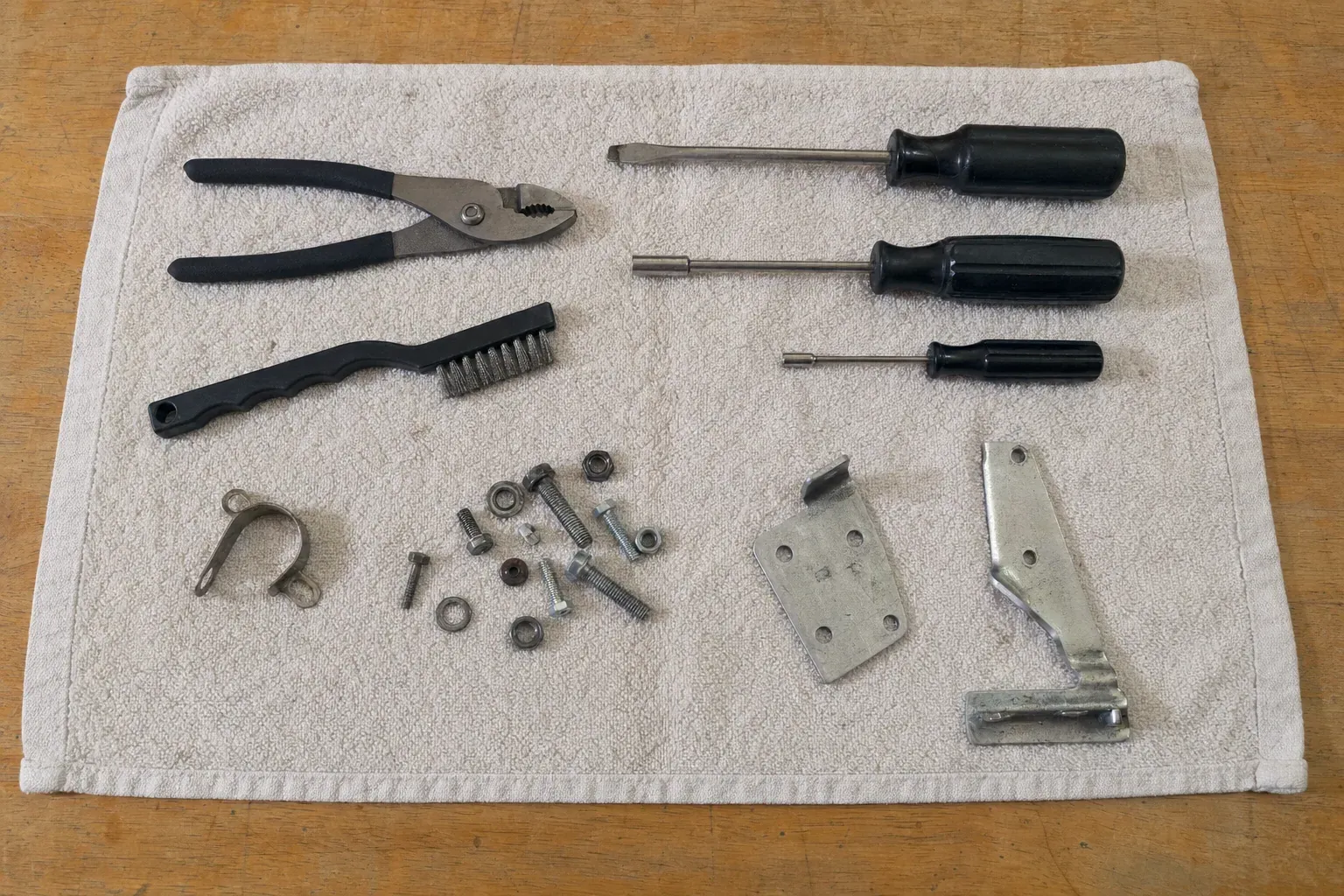 Black-handled screwdrivers, pliers, brush, brackets and bolts on towel
