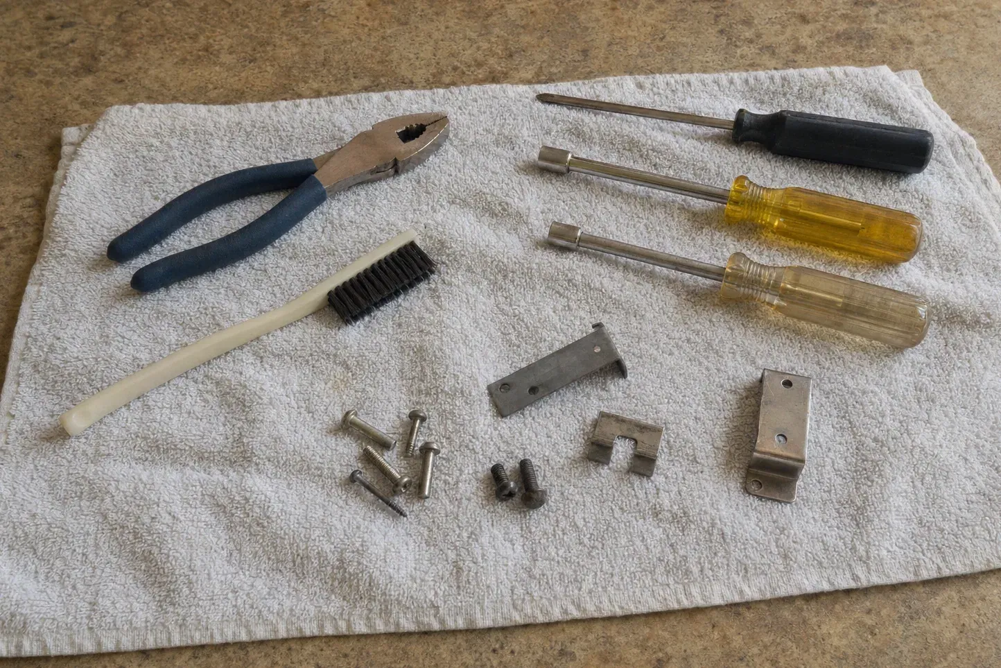 Nut drivers, pliers, brush, brackets and screws on white towel