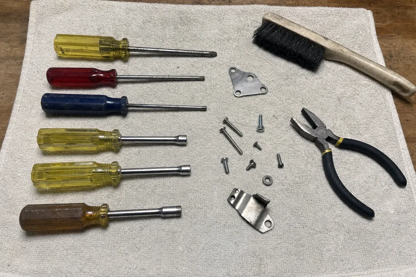 Brush, pliers, six screwdrivers, bracket and assorted screws on towel