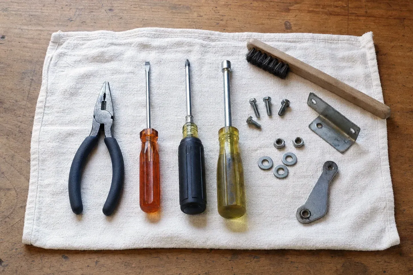 Wire brush, brackets, nuts, three screwdrivers and pliers on cloth