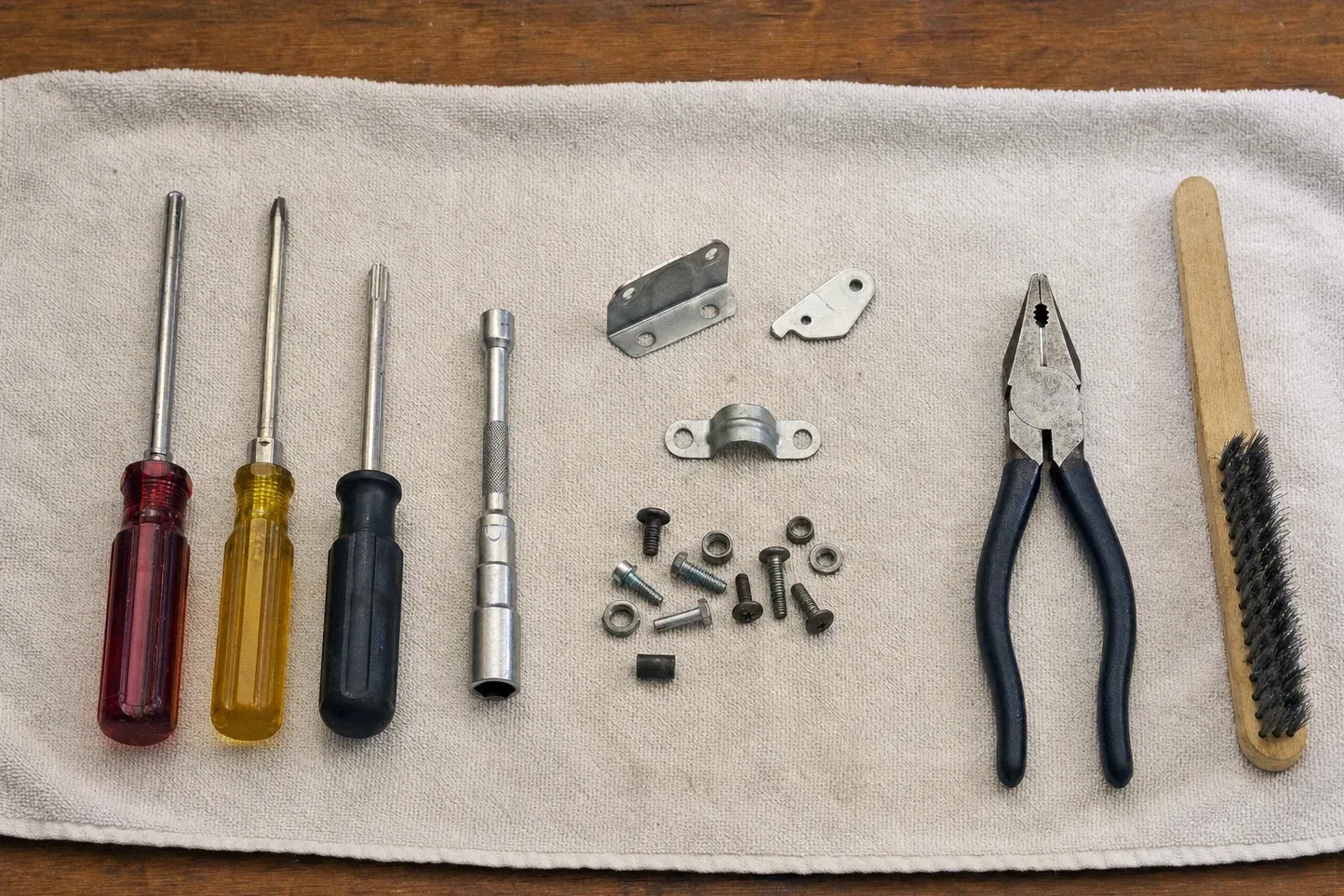 Wire brush, pliers, brackets, screws and four screwdrivers on towel