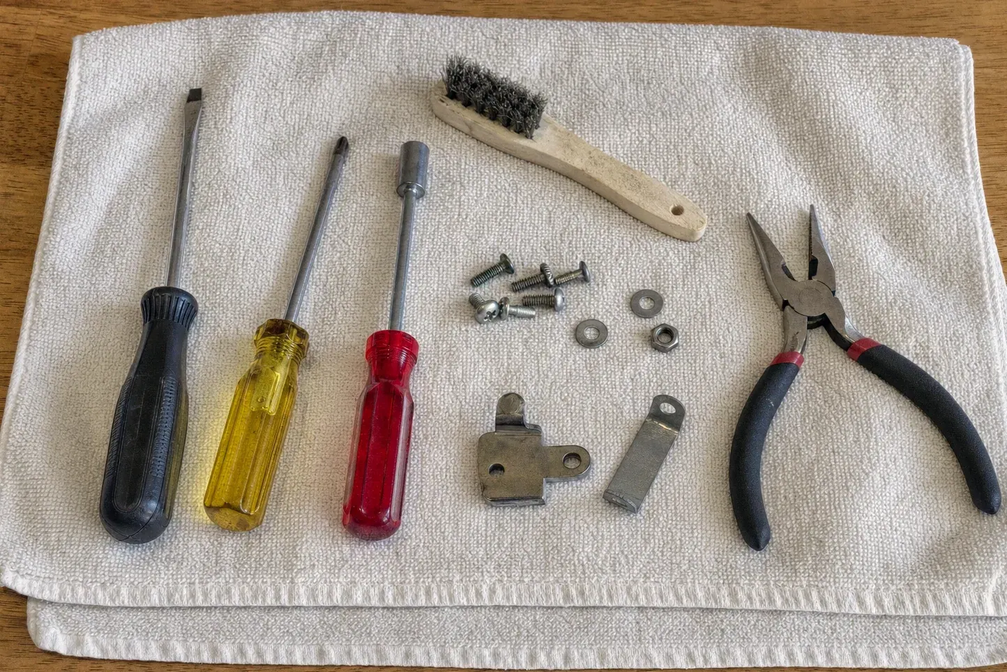 Pliers, screwdrivers, wire brush, screws and brackets on white towel