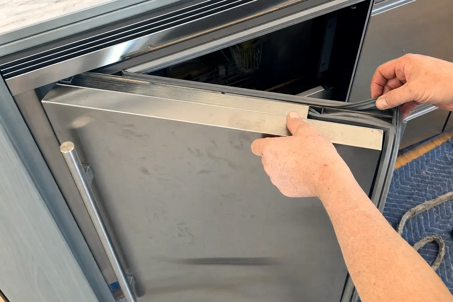 Hands pulling a door gasket from a stainless dishwasher door panel